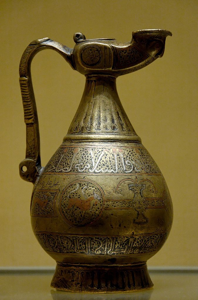 Art of the Seljuk Empire: Ewer with inscriptions in animated kufic and simple kufic. Copper alloy with engraved decoration inlaid with silver and red copper, Iran, late 12th century.Louvre Museum